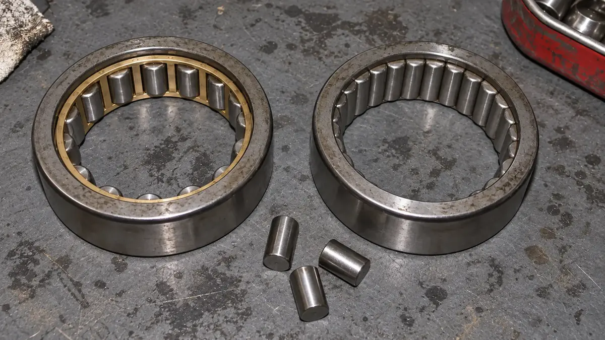 Two cylindrical roller bearing outer rings of identical size side by side, the left one with a machined brass cage holding a gap of daylight either side of every roller, the right one with no cage at all and its rollers touching, fitting roughly twice as many in the same ring