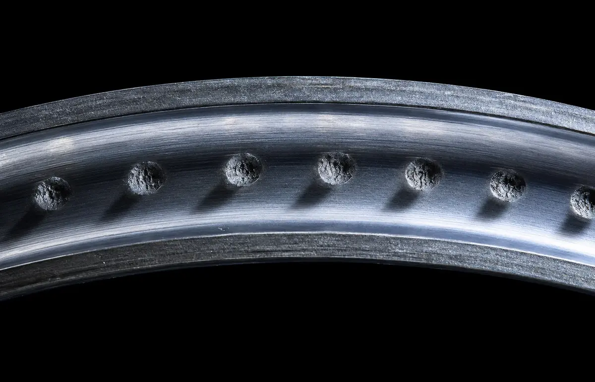 Macro photograph of a bearing inner-ring raceway showing a row of evenly-spaced ball-shaped indentations from a static-overload brinelling event