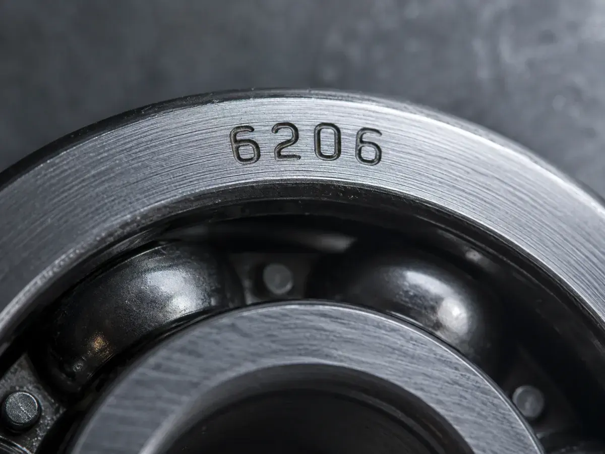Macro close-up of the outer ring face of a deep groove ball bearing showing the stamped designation 6206 standing out in relief under low-angle lighting