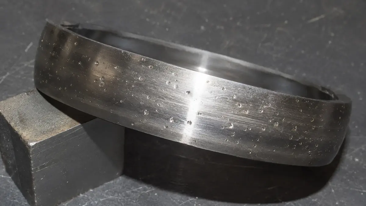 Particle indentations on a bearing raceway, the irregular dents left by hard contaminants in the lubricant that produce non-periodic contaminant noise