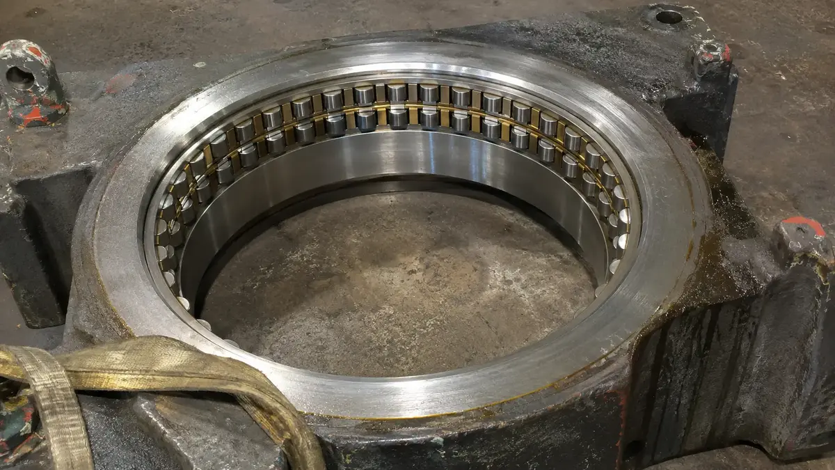 A four-row cylindrical roller bearing seated in the bore of a cast mill chock, the outer ring contacting the housing all the way round with the machined brass cage and its rollers inside it, the assembly that is eased over a roll-mounted inner ring during a roll change
