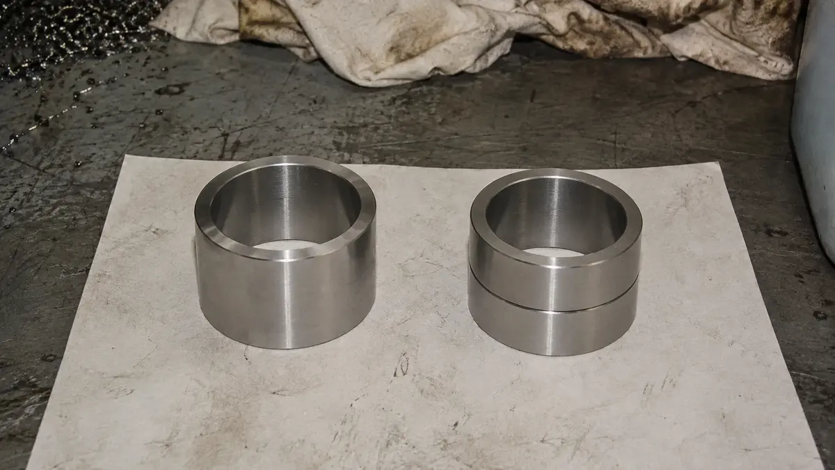 Two inner-ring forms for a four-row cylindrical roller bearing side by side on an inspection bench: a one-piece unflanged sleeve on the left, and on the right a split pair of the same total width whose butt joint is what lets an FCD design be mounted on a larger roll neck