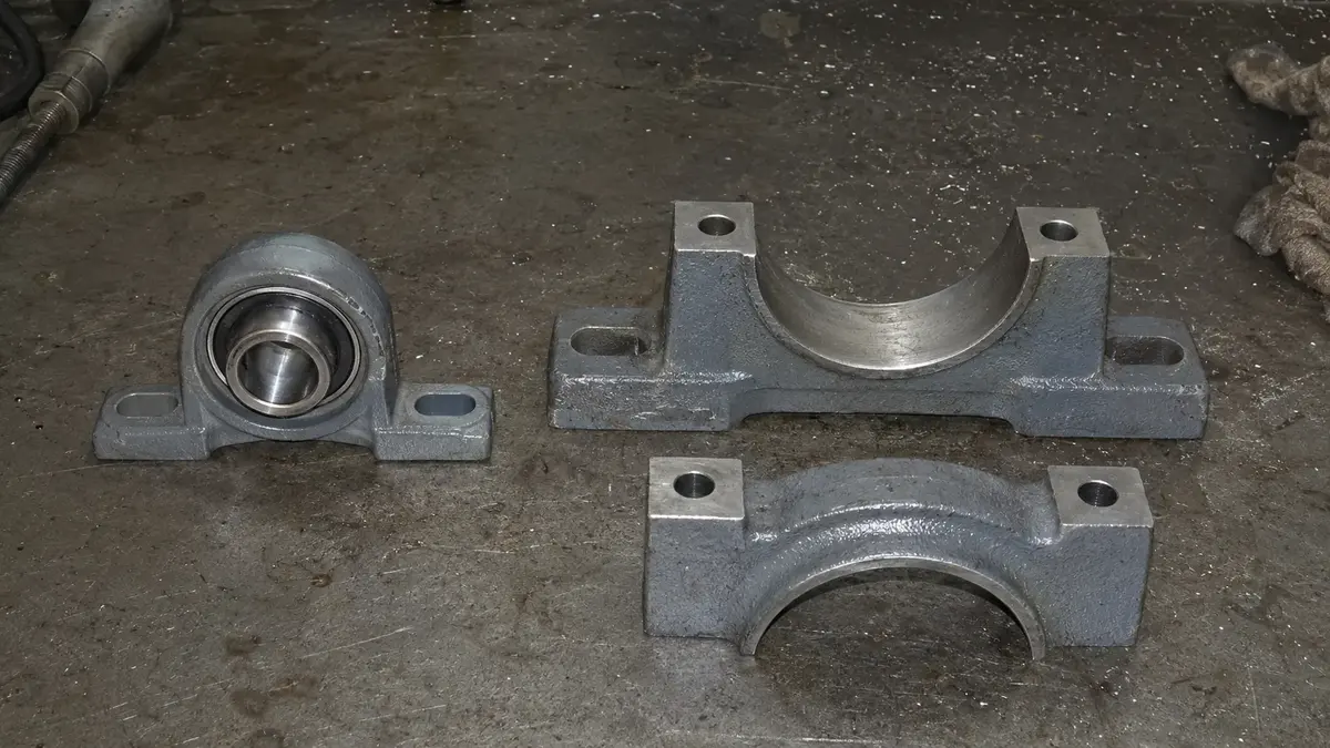 A small one-piece insert-bearing pillow block unit beside a larger two-piece split plummer block housing with its cap lifted off the base, showing the serviceable split-housing construction that a sealed insert unit does not offer